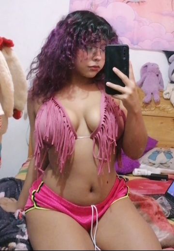 Woman with curly violet hair taking a mirror selfie in a pink fringe top